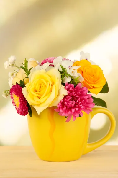 Belo buquê de flores brilhantes na caneca a cores, na mesa de madeira, no fundo brilhante — Fotografia de Stock