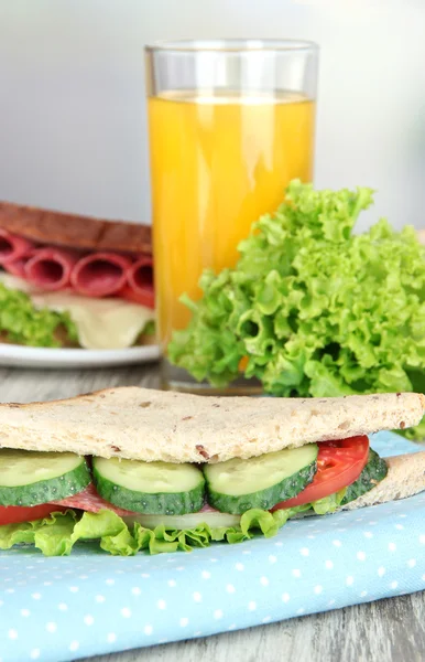 Композиция с фруктовым соком и вкусным сэндвичем с колбасой из салями и овощами на цветной салфетке, на деревянном столе, на ярком фоне — стоковое фото