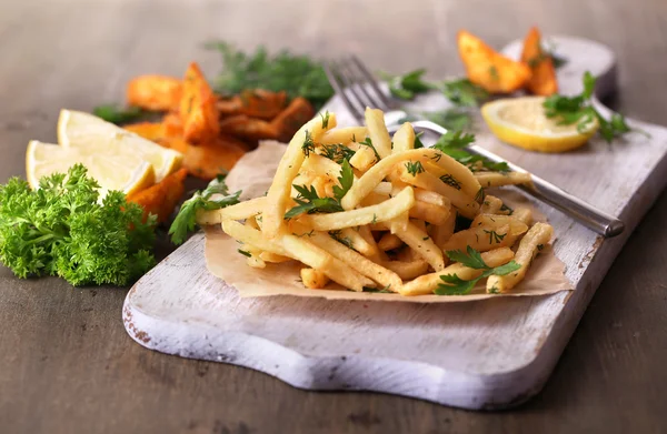 French fries on tracing paper on board on wooden table — Stock Photo, Image