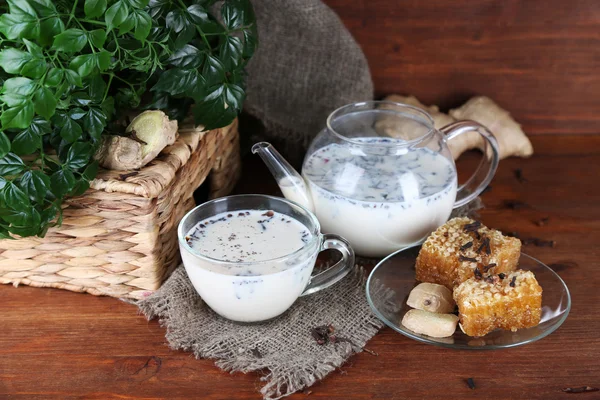 Teekanne und Tasse Tee mit Milch und Gewürzen auf Sacktuch von Holztisch auf hellem Hintergrund — Stockfoto
