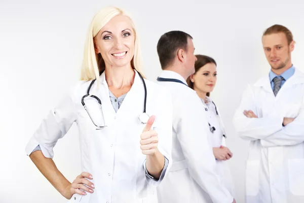 Doktor stojící před spolupracovníky na šedém pozadí — Stock fotografie