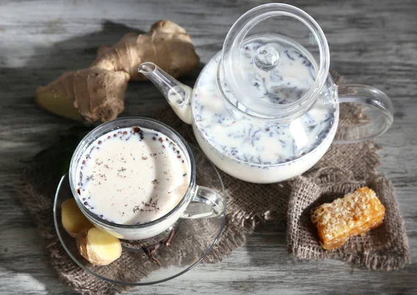 Konvice a šálek čaje s mlékem a kořením na pytloviny dřevěný stůl — Stock fotografie