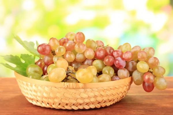 Raisin sucré mûr dans un panier sur une table en bois, sur fond nature — Photo