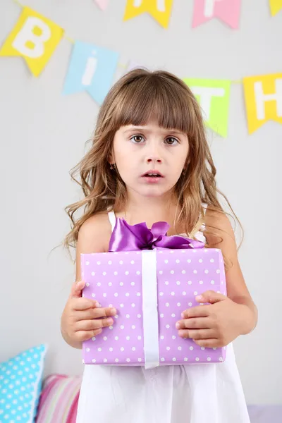 Маленька дівчинка з подарунком у кімнаті на сірому фоні стіни — стокове фото