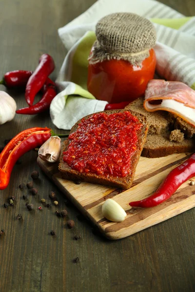 Composition with salsa sauce on bread,, red hot chili peppers and garlic, on napkin, on wooden background — Stock Photo, Image