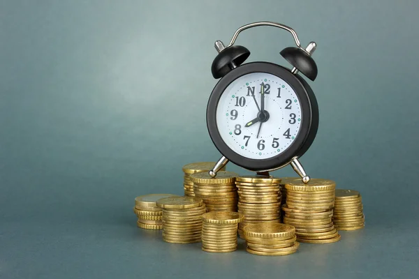 Relógio despertador com moedas em fundo cinza — Fotografia de Stock