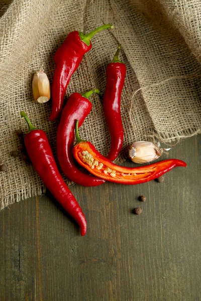 Chiles rojos picantes y ajo, sobre tela de saco, sobre fondo de madera — Foto de Stock