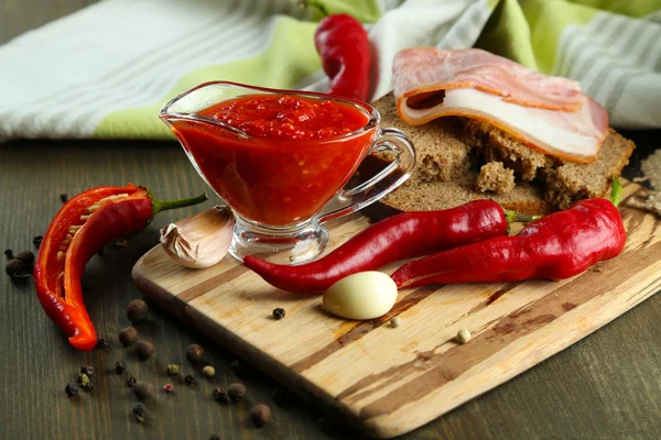 Composition with salsa sauce on bread,, red hot chili peppers and garlic, on napkin, on wooden background — Stock Photo, Image