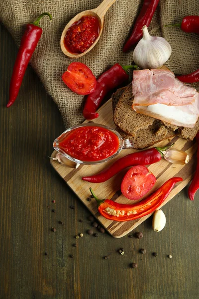 Состав с соусом сальсы на хлебе,, красный острый перец чили и чеснок, на мешковине, на деревянном фоне — стоковое фото