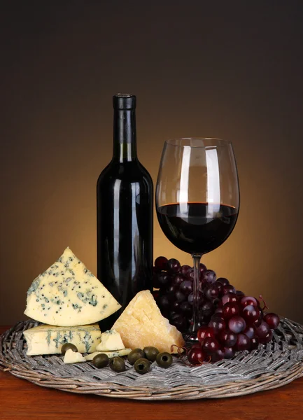 Nature morte raffinée de vin, fromage et raisins sur plateau en osier sur table en bois sur fond brun — Photo