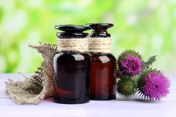 Medizinflaschen mit Distelblumen auf Naturhintergrund — Stockfoto
