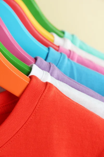 Camisas diferentes em cabides coloridos no fundo bege — Fotografia de Stock
