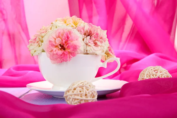 Roses in cup on wooden table on pink cloth background — Stock Photo, Image