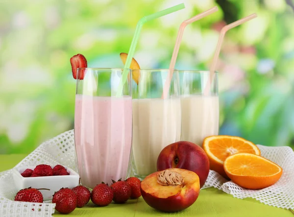 Delicious milk shakes with strawberries and peach on wooden table on natural background