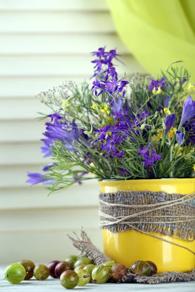 Mooi boeket van wilde bloemen in cup en bessen op houten tafel — Stockfoto