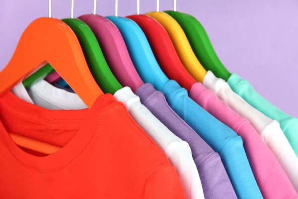 Camisas diferentes em cabides coloridos no fundo roxo — Fotografia de Stock