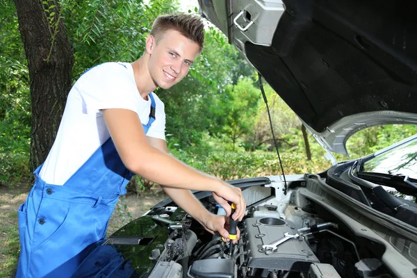 Молодой автомеханик ремонтирует автомобильный двигатель на открытом воздухе — стоковое фото