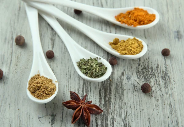 Assortment of spices in white spoons, on wooden background