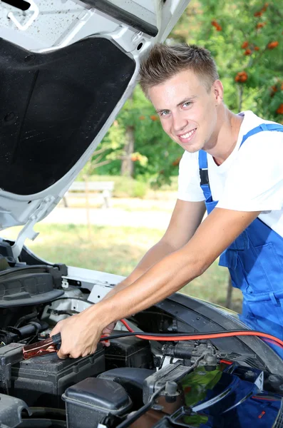 Mecânico de carro jovem usa cabos jumper bateria para carregar bateria morta — Fotografia de Stock