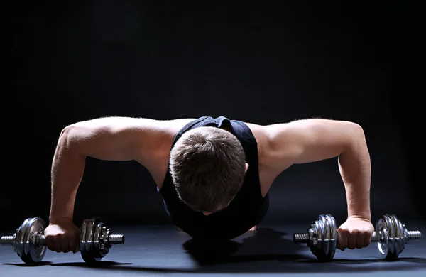 Knappe jonge gespierde sportman uitvoeren oefening met halters op donkere achtergrond — Stockfoto