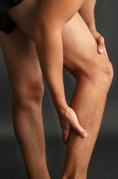 Молодой человек с болью в ногах на сером фоне — стоковое фото