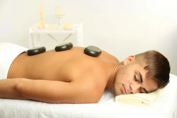 Young man relaxing with hot stones on back before massage — Stock Photo, Image