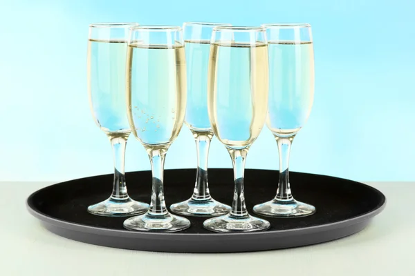 Muitos copos de champanhe na bandeja na mesa, no fundo azul — Fotografia de Stock
