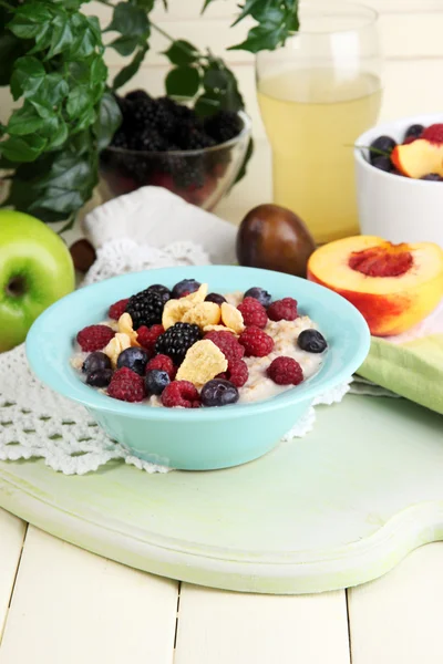 Oatmeal in plate with berries on napkins on wooden board on table on bright background — Stock Photo, Image