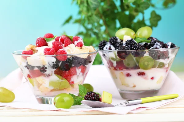 Fruit salad in glass bowls, on wooden table, on bright background — Stock Photo, Image