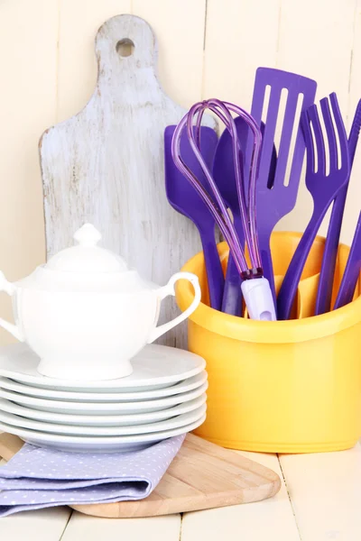 Пластиковые кухонные принадлежности в чашке на деревянном столе — стоковое фото