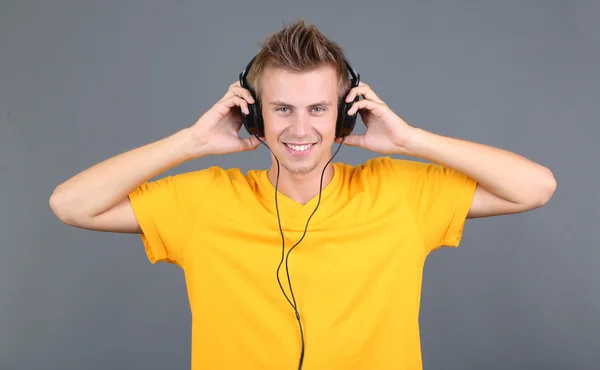 Schöner junger Mann hört Musik auf grauem Hintergrund — Stockfoto