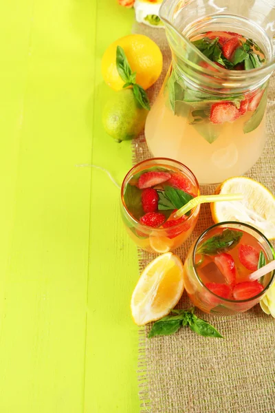 Limonata di basilico con fragola in brocca e vetro, su tavolo di legno, su sfondo brillante — Foto Stock