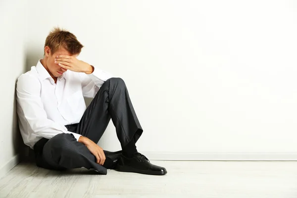 Jovem empresário sentado no chão, no fundo da parede cinza — Fotografia de Stock