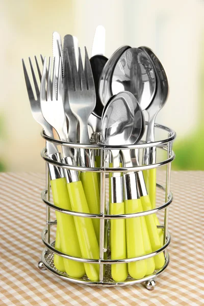 Knives, forks and spoons in metal stand on tablecloth on bright background — Stock Photo, Image