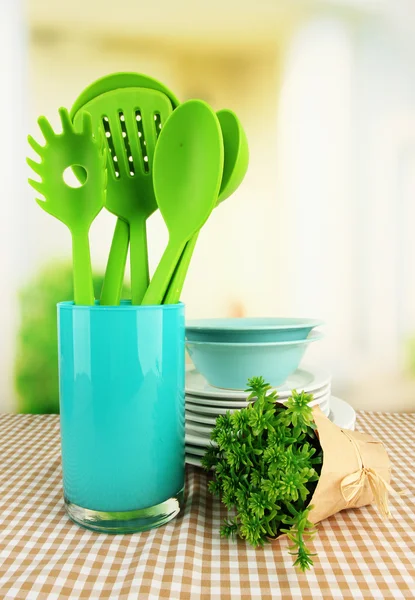 Plastic kitchen utensils in stand with clean dishes on tablecloth on bright background — Stock Photo, Image