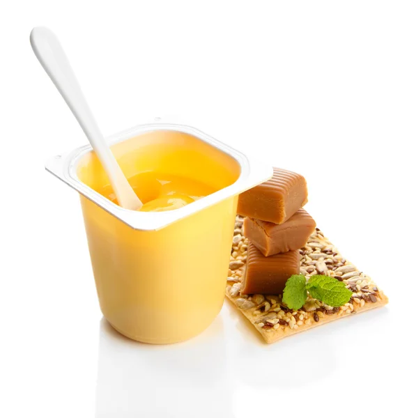 Iogurte saboroso em copo de plástico aberto, biscoitos e doces de toffee isolados em branco — Fotografia de Stock