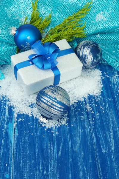 Composition with Christmas balls, gift box and snow on color wooden background — Stock Photo, Image