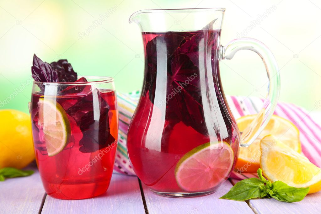 Red basil lemonade in jug and glass, on bright background
