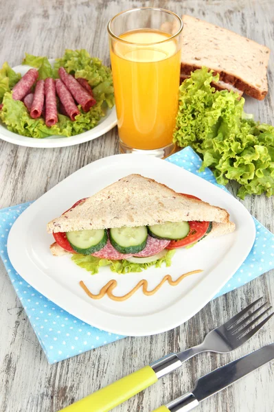 Compositie bij vruchtensap en lekkere sandwich met worst salami en groenten op kleur servet, op houten tafel achtergrond — Stockfoto