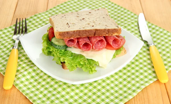 Sanduíche saboroso com salsicha de salame e legumes na placa branca, no fundo de madeira — Fotografia de Stock