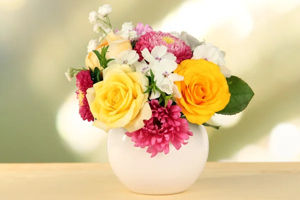 Hermoso ramo de flores brillantes en jarrón de color, sobre mesa de madera, sobre fondo brillante — Foto de Stock