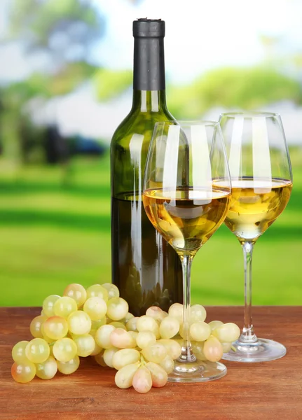 Ripe grapes, bottle and glasses of wine, on bright background — Stockfoto