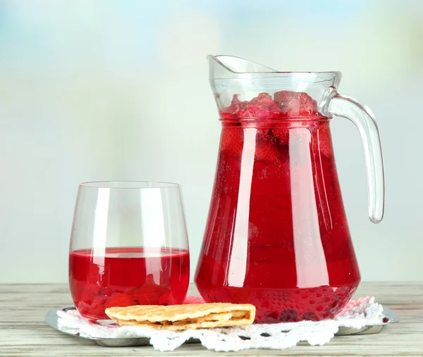 Pitcher and glass of compote on napkin on wooden table on light background — Stock Photo, Image
