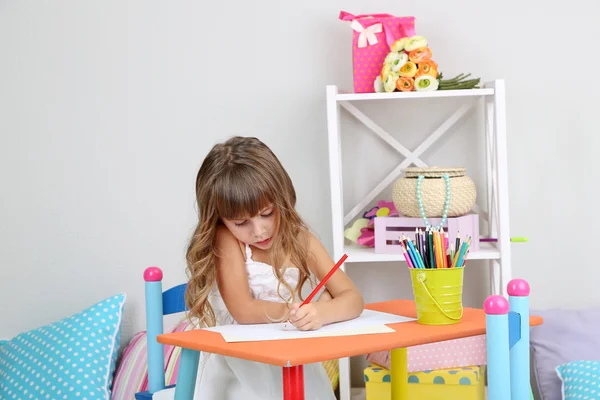 Dziewczynka rysuje siedzi przy stole w pokoju na ścianie szary tło — Zdjęcie stockowe