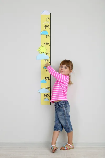 Kleines Mädchen misst Höhe gegen Wand im Zimmer — Stockfoto