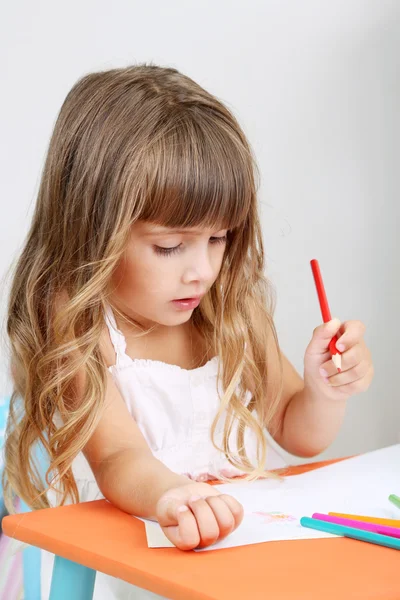 Menina desenha sentado à mesa no quarto no fundo da parede cinza — Fotografia de Stock