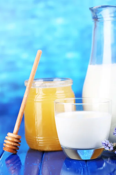 Honung och mjölk på träbord på blå bakgrund — Stockfoto