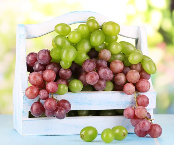 Raisins mûrs verts et violets dans le panier sur table en bois sur fond naturel — Photo