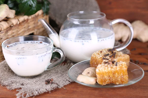 Tekanna och kopp te med mjölk och kryddor på säckväv av träbord på ljus bakgrund — Stockfoto