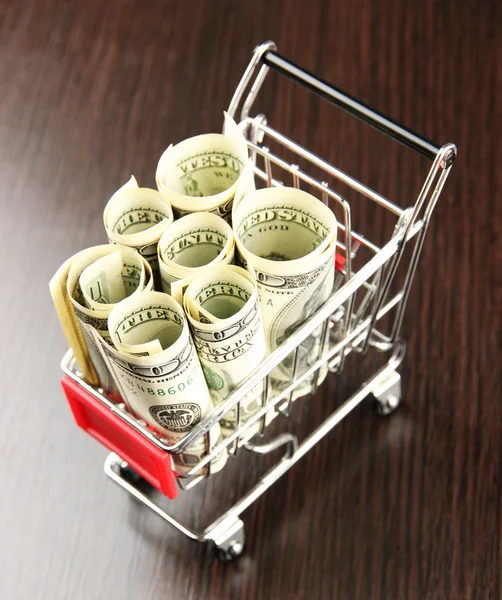 Shopping trolley with dollars, on dark background — Stock Photo, Image
